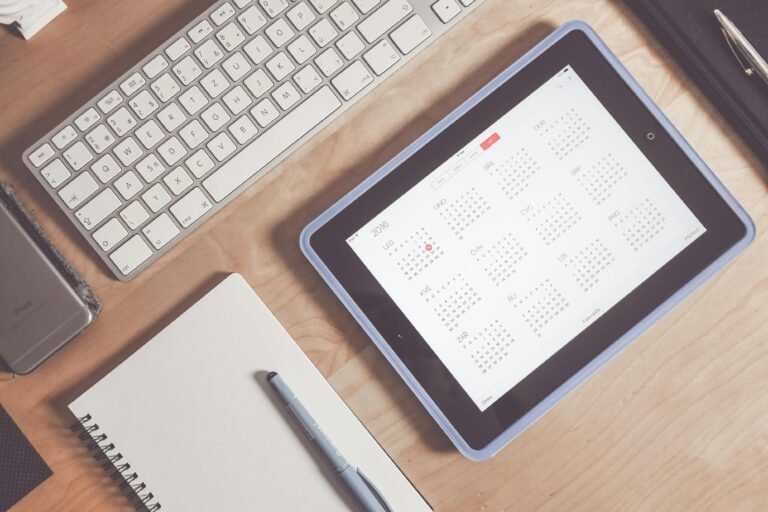 A tidy desk setup featuring a tablet displaying a calendar, keyboard, and stationary items.