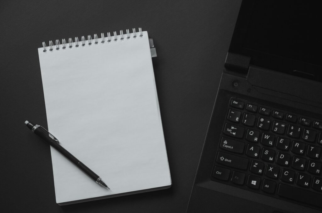 Flat lay of an office workspace with a laptop, notepad, and mechanical pencil on a black background.